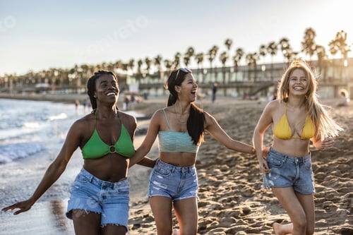 Preview: Group of beautiful young multiracial women strolling on the beach.Three friends walking on the beach