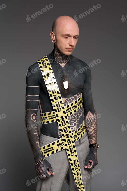 Preview: bare-chested man with tattoos and police line around body looking down isolated on grey