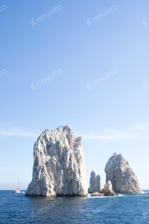Preview: an ocean view with two large rocks in the water and small boats