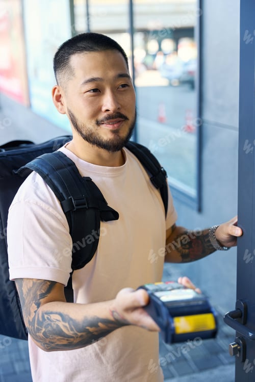 Preview: Young delivery guy opening the door and holding terminal