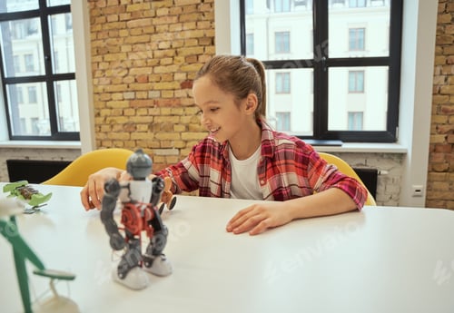 Preview: Happy little girl smiling while sitting at the table and playing with technical toy, spending time