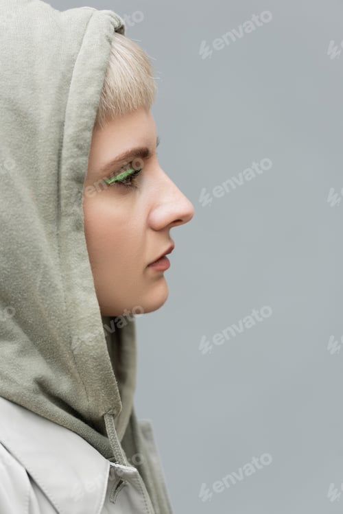 Preview: side view of stylish and young woman with bangs, green eye shadows and blonde hair standing