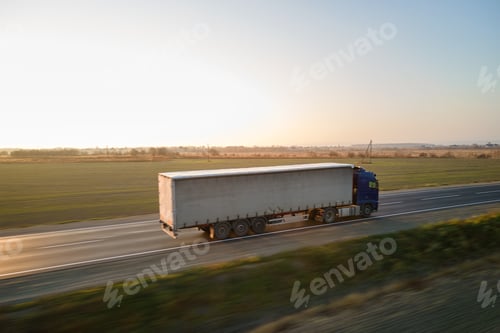 Preview: Aerial view of semi-truck with cargo trailer driving on highway hauling goods in evening.