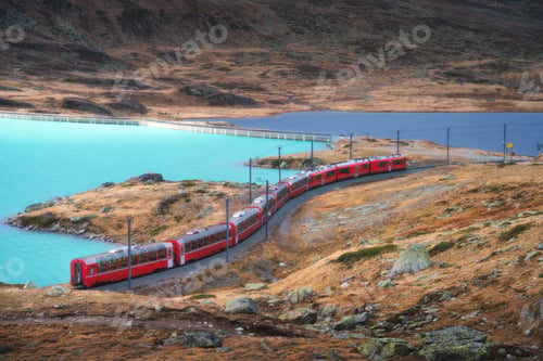 Preview: Aerial view of red train near alpine mountain lake and cloudy sk