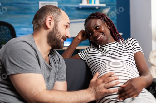 Preview: Cheerful pregnant multiethnic young couple smiling at each other