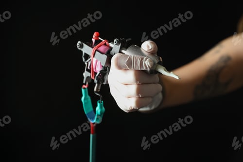 Preview: Tattoo artist with professional machine on black background, closeup