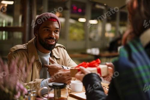 Preview: Multinational couple smiling and holding gift box in cafe outdoors