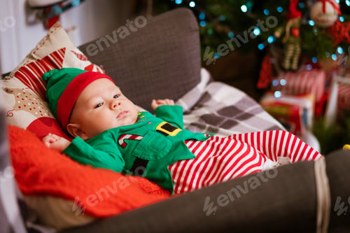 Preview: Beautiful half-year-old child lies on pillows and smiles in a red-green costume
