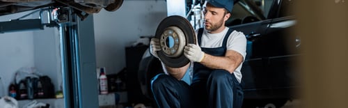 panoramic shot of handsome car mechanic looking at metallic car brake