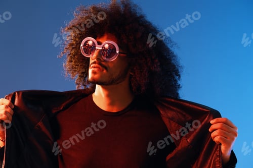 Preview: Portrait of a stylish man with curly hair with glasses smile on blue background multinational, color