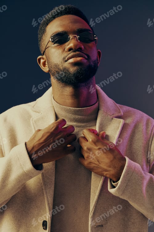 Vista previa: Stylish African man posing confidently in sunglasses and a beige coat against a colorful background