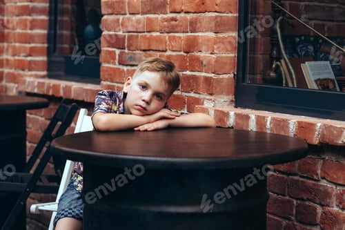 Preview: Pensive Boy Leans on Round Table Outside