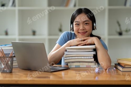 Preview: Asian woman in headphones sitting on stack of books and laptop researching and relaxing listening to