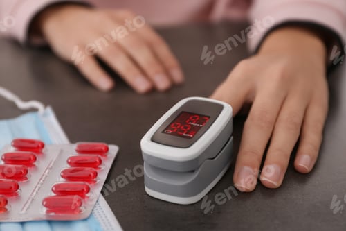 Preview: Woman measuring oxygen level with modern fingertip pulse oximeter at grey table, closeup
