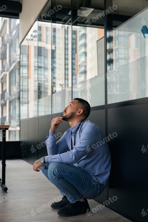 Preview: Pensive company worker seated against wall staring up