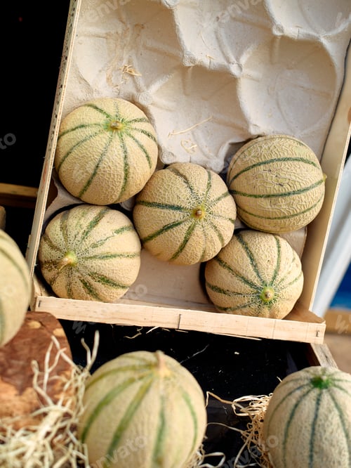 Preview: Fresh cantaloupes neatly stacked in a wooden crate at a farmers market.