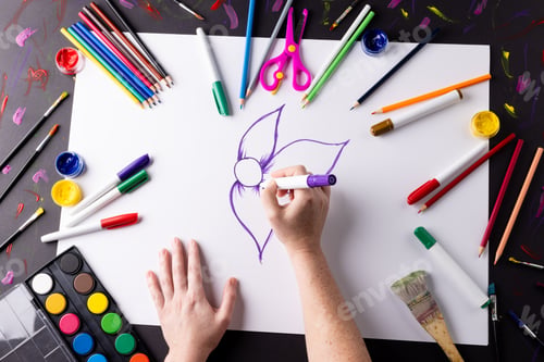 Preview: Overhead of hands drawing purple flower on paper, with art materials on table top