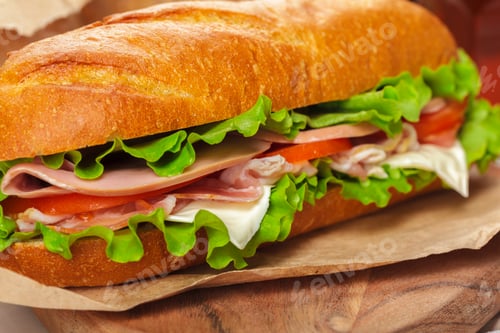 Preview: Fresh sandwich with vegetables and meats on a wooden table in bright light