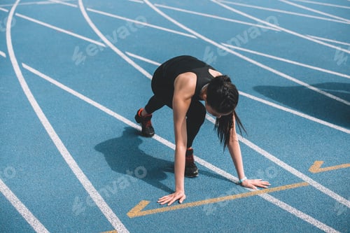 Preview: Concentrated young sportswoman in starting position on running track stadium
