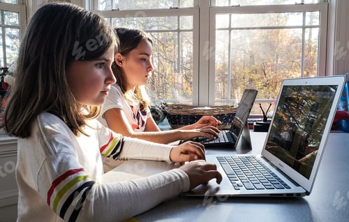 Preview: Generation z kids using technology for school work with light and shadows through a window.