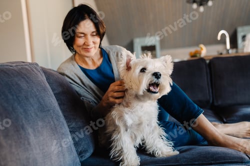 Preview: White mature woman petting her dog while sitting on couch
