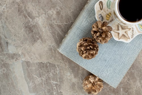 Preview: Cup of aromatic coffee on top of book with pinecones