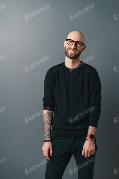 Preview: Young smiling man with beard and glasses on gray studio background
