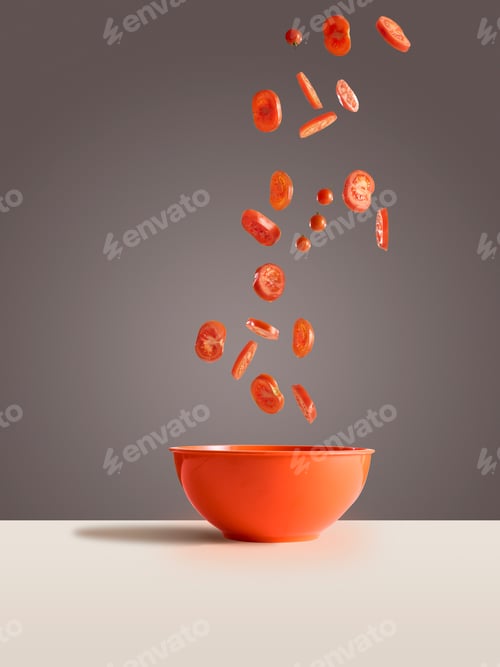 Preview: Sliced tomatoes tumbling into an orange bowl on a neutral background