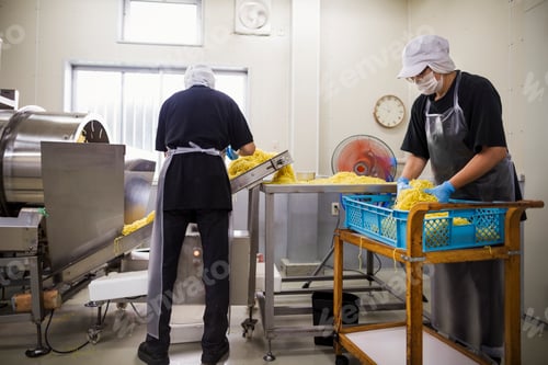 Preview: Workers in aprons and hats collecting freshly cut noodles from the conveyor belt.
