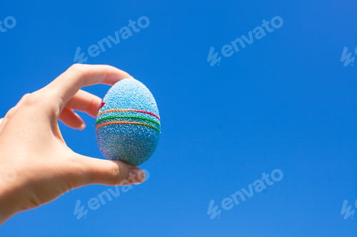 Preview: Bright Beautiful Easter egg in hand on background of blue sky