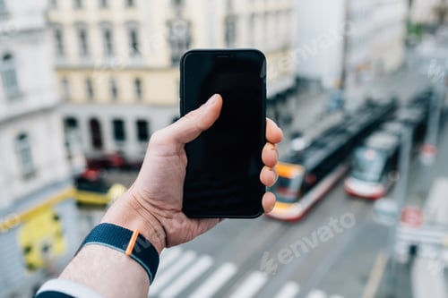 Preview: Closeup shot of a hand holding a mobile phone on the street road background