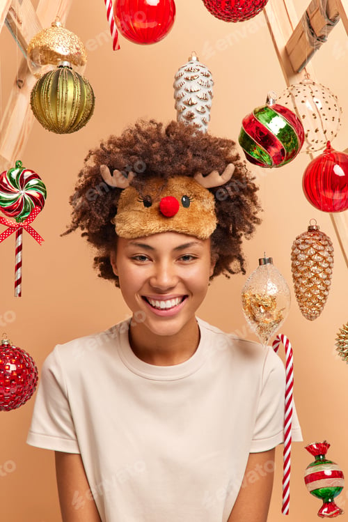 Preview: Positive dark skinned woman wears deer sleep mask and casual t shirt smiles broadly waits for winter
