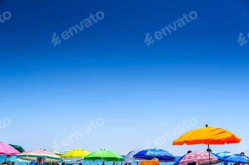 Preview: Colorful beach umbrella stuck in the sand surrounded by a group of bathers in summer