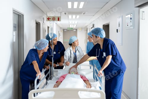 Preview: Diverse group of healthcare workers pushing patient in bed down hospital corridor