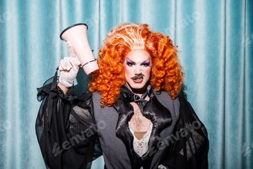 Preview: Drag Queen Performer With Ornate Orange Curls Holding a Megaphone in a Lively Drag Show Setting