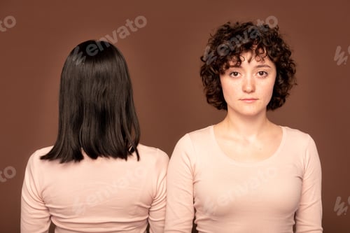 Preview: Young serious brunette woman standing on background of back of another female