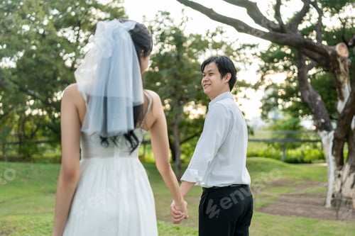 Preview: Asian young married couple holding hand each other in park during sunset.