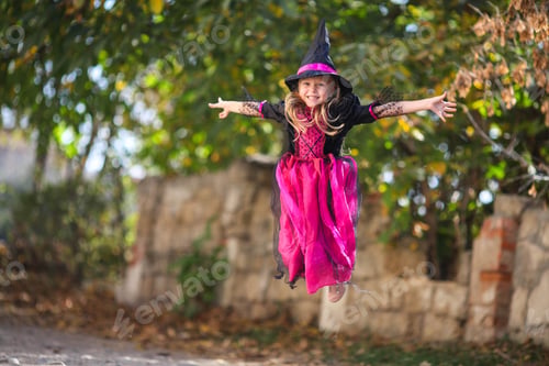 Preview: A little girl in a witch costume is jumping on the street. Halloween holiday. Copy space