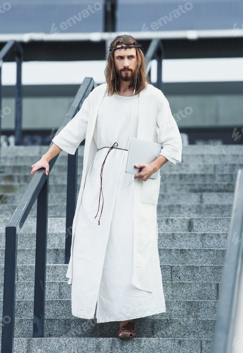 Preview: serious Jesus in robe and crown of thorns walking on stairs with laptop and listening music in city