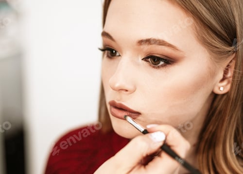 Preview: makeup artist paints lips with lipstick with a brush on a beautiful young woman blonde model