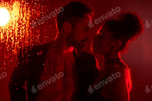 Preview: A passionate embrace of a loving couple against a red backdrop with rain on the glass