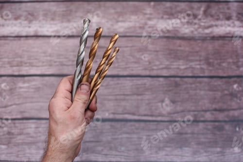 Preview: close-up drill bits in hand. smeared hand of worker with drill bits. lettering