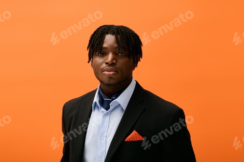 Preview: Stylish young man poses confidently against a vibrant orange background during a fashion event