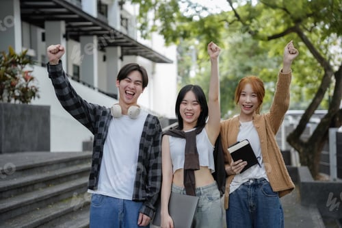 Preview: Three young students celebrate success outside university building, raising fists in excitement