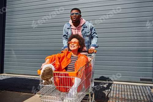 Preview: Excited young african american man in sunglasses and denim jacket standing near smiling best friend