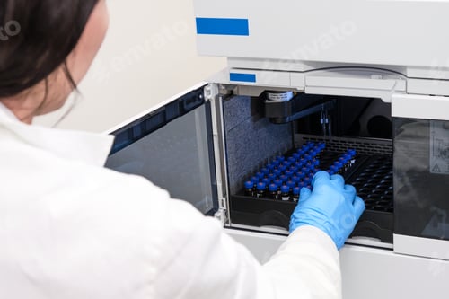 Preview: Scientist in a white lab coat putting vial with a sample into autosampler of HPLC system. High