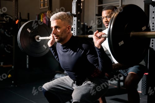 Preview: Man weightlifting in gym with personal trainer spotting
