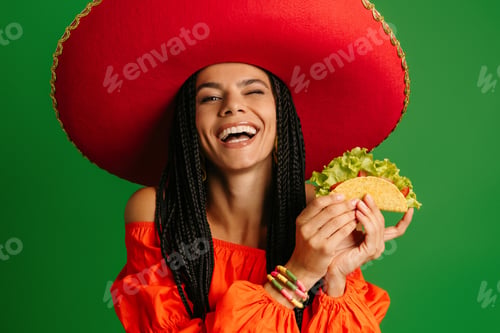Preview: Happy young Mexican woman in Sombrero holding taco and smiling against green background
