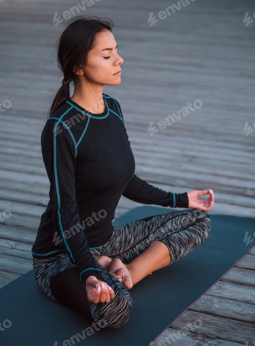 Preview: Concentrated girl in black practicing in yoga meditation on wooden seafront.
