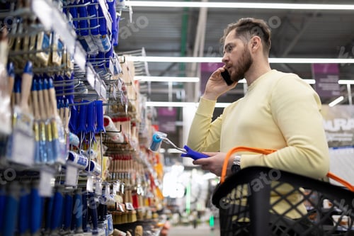 Preview: a man in a hardware store chooses paint brushes while discussing it on the phone with his wife